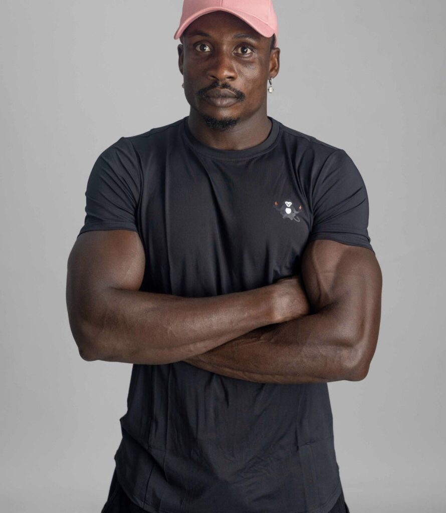 Portrait of Zodsolo with arms folded, wearing a black AfroAlien Fit t-shirt with the meditating monkey logo and a pink cap.