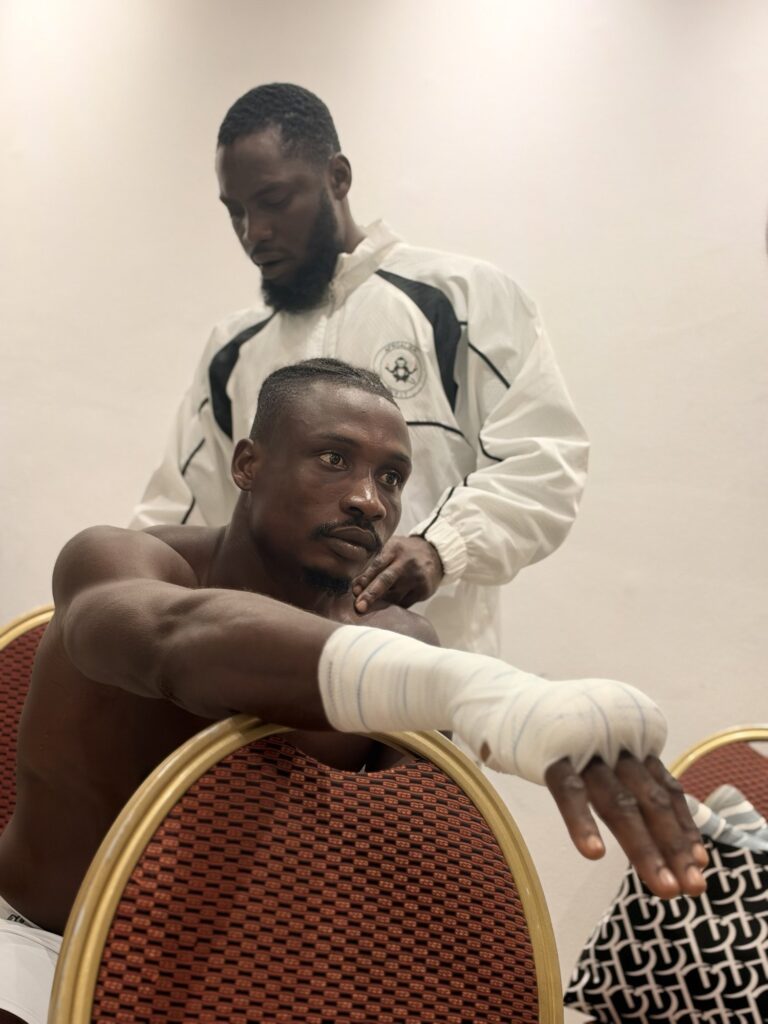 Zodsolo, hands wrapped, gets ready backstage with a team member in an AfroAlien jacket.