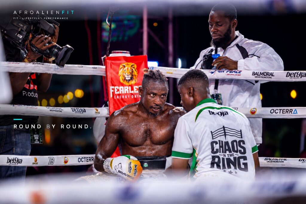 Zodsolo listens to his corner between rounds at Chaos in the Ring, in an AfroAlien Fit "Round by round" graphic.